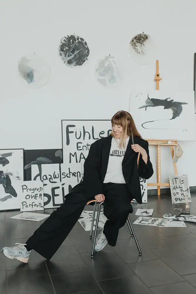 Frau in Kunststudio mit abstrakten Wandbildern und Malutensilien, kreative Atmosphäre.