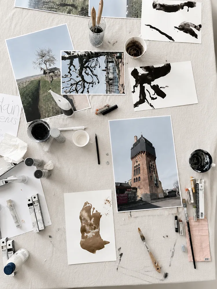 Kreatives Mal-Setup mit Fotos, Pinseln und Farben auf einem großen Tisch ausgebreitet